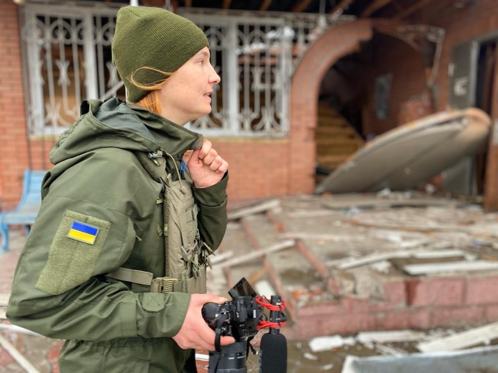 Helena Maksyom filming with a camera near a shelled building